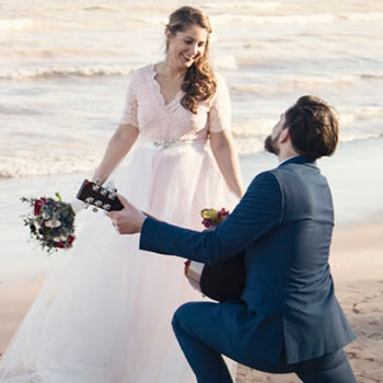 groom plays guitar for bride on a beach, captured by a wedding videographer